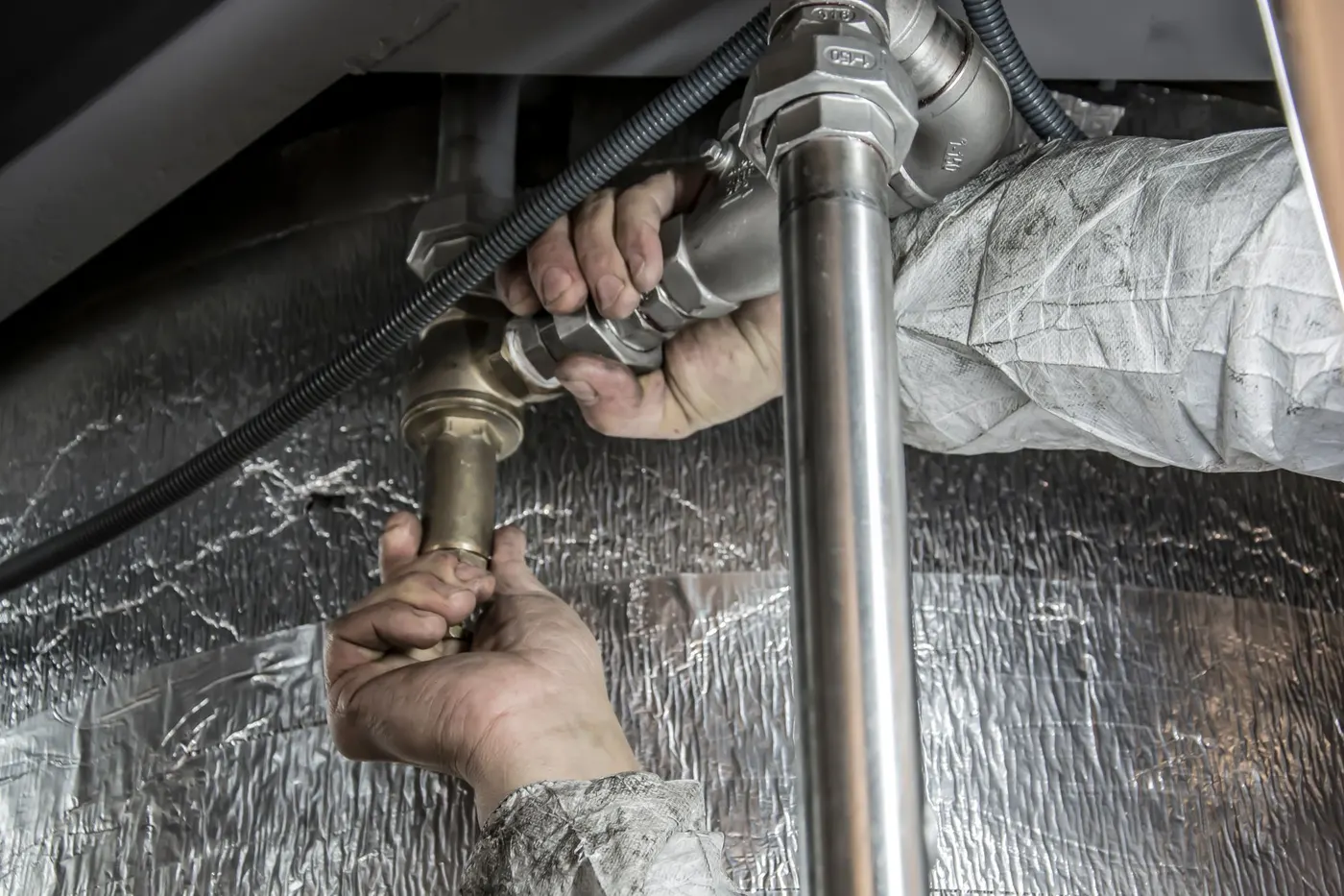 Engineer working on pipework and valves beneath a hot water system